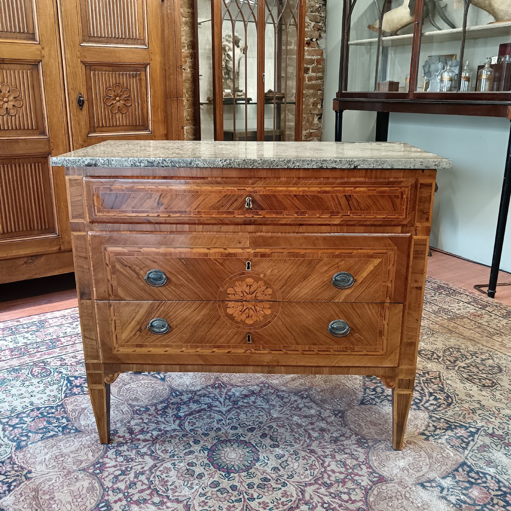 An eighteenth-century Italian Neoclassical marquetry commode with three drawers, geometric timber inlays, a grey marble top, and tapered square legs.
