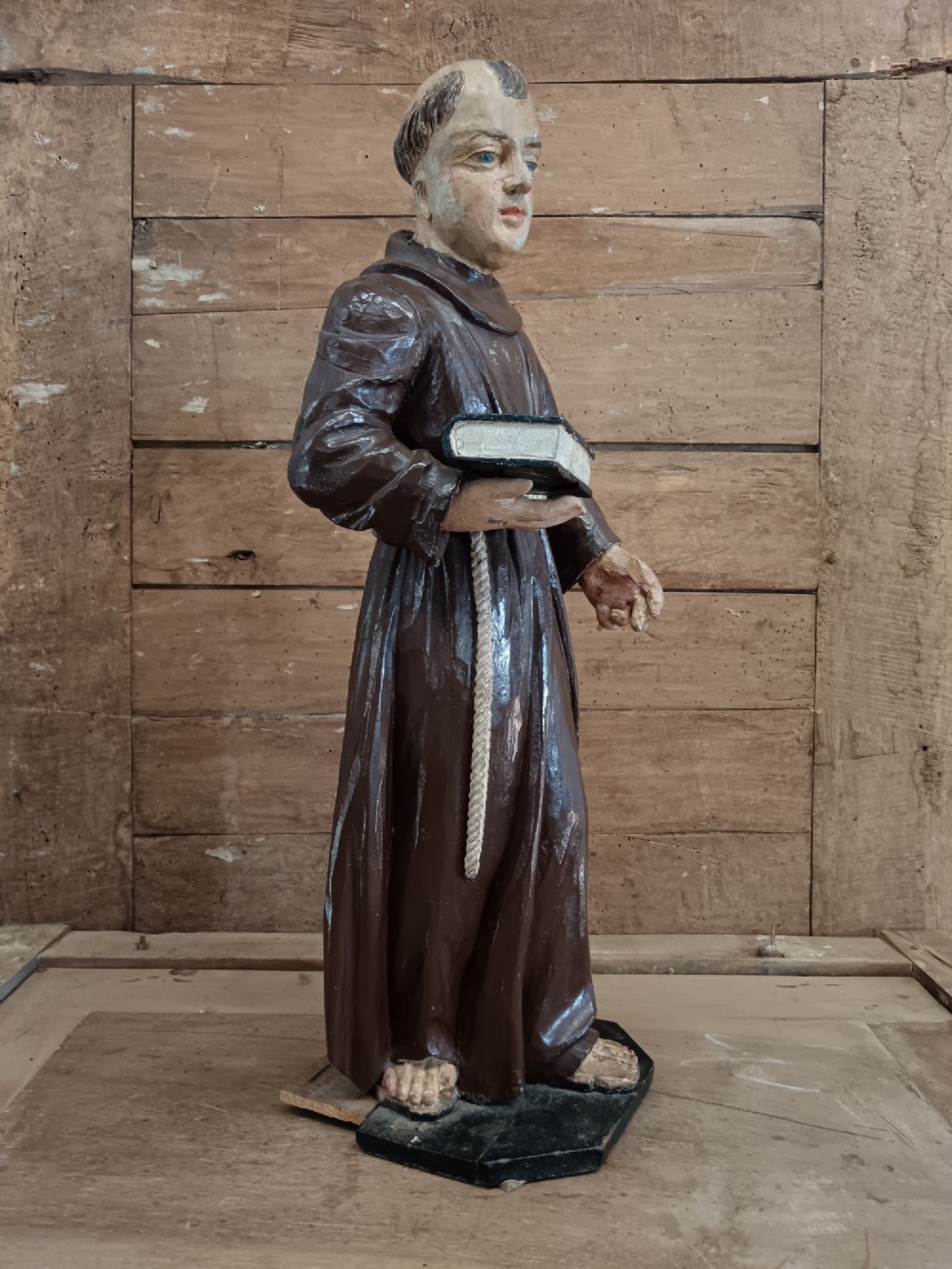 An antique carved wooden figure depicting Saint Anthony wearing a dark brown habit and holding a book. View II