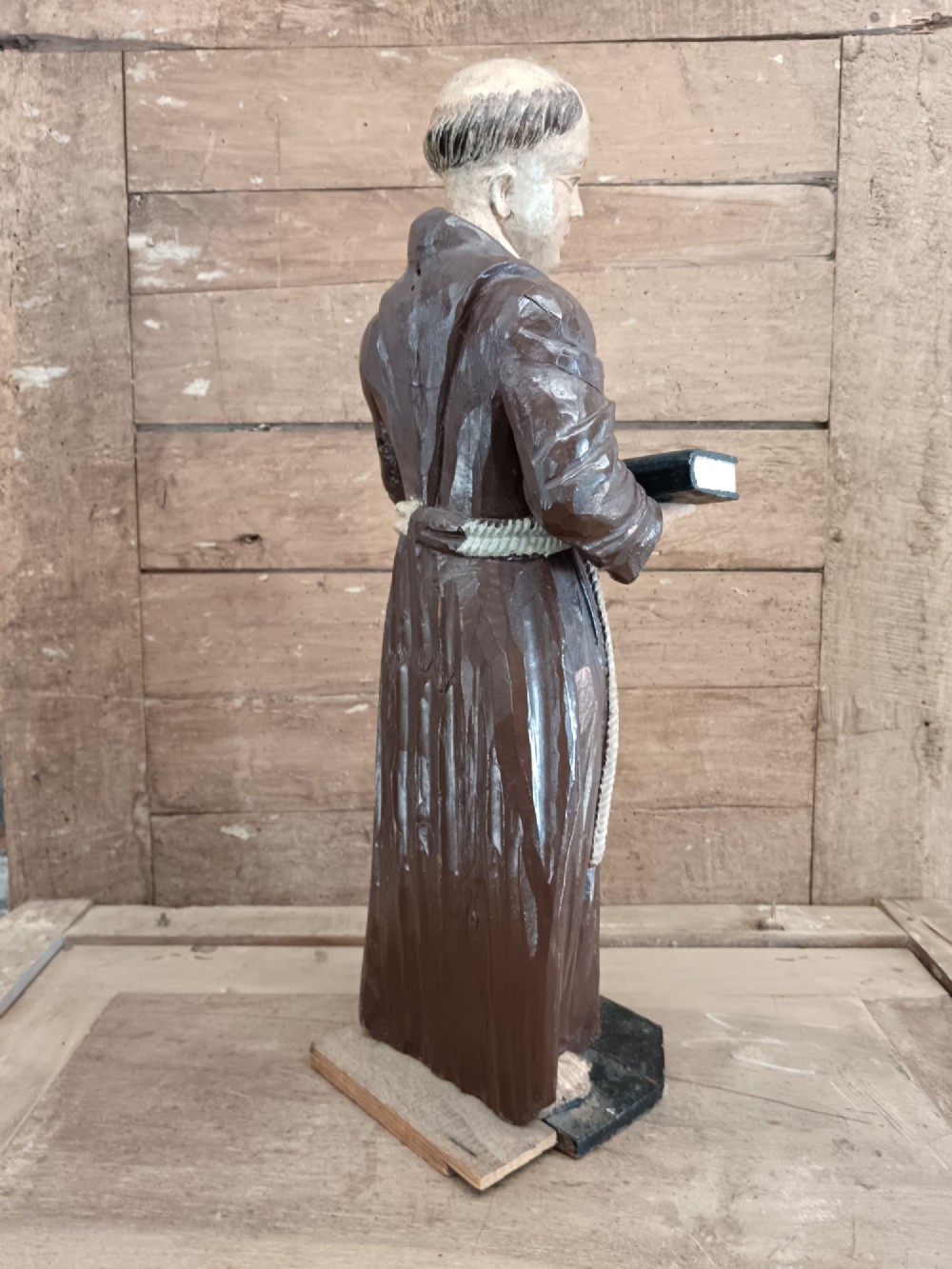 An antique carved wooden figure depicting Saint Anthony wearing a dark brown habit and holding a book. View III