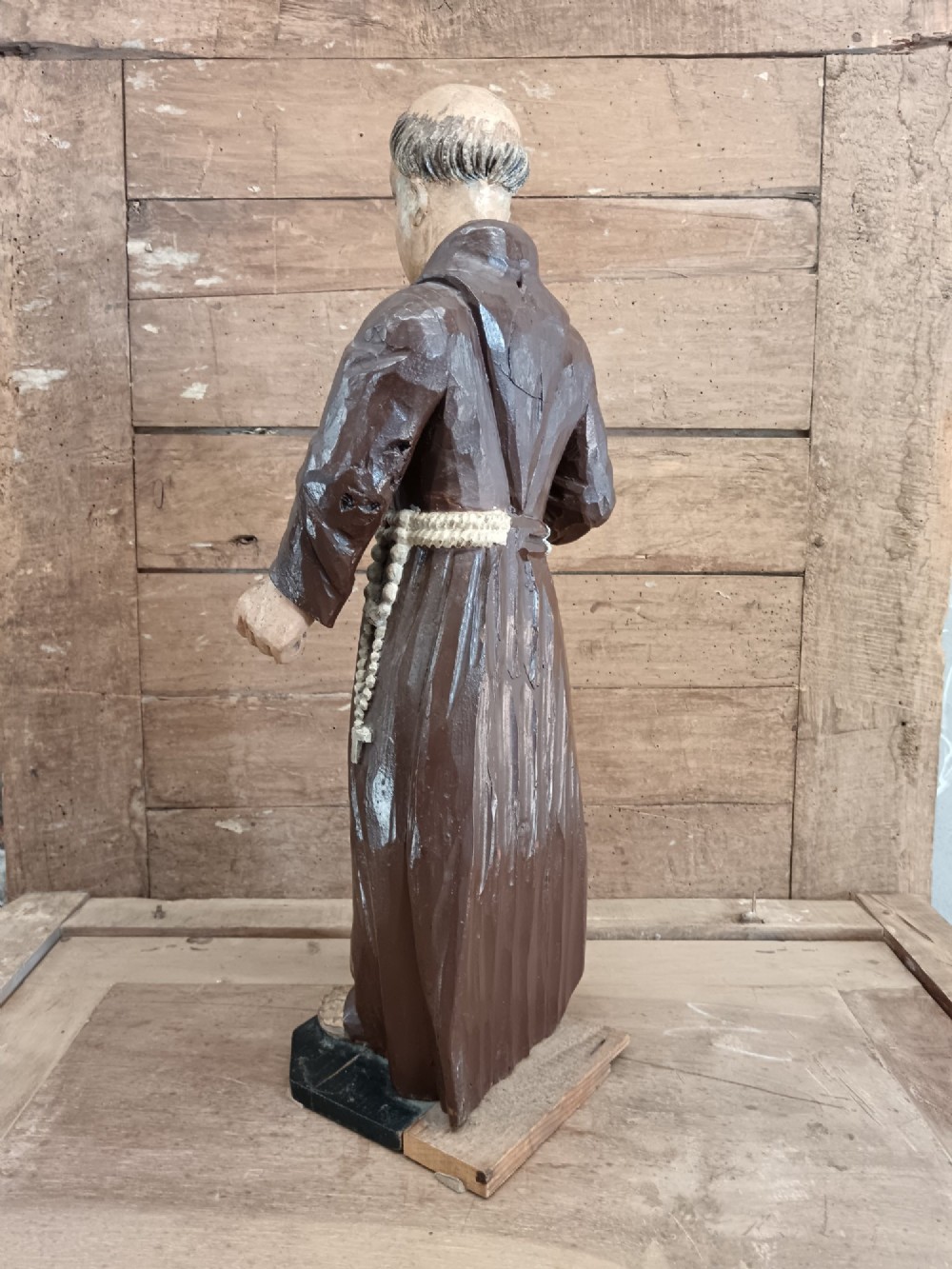 An antique carved wooden figure depicting Saint Anthony wearing a dark brown habit and holding a book. View IV