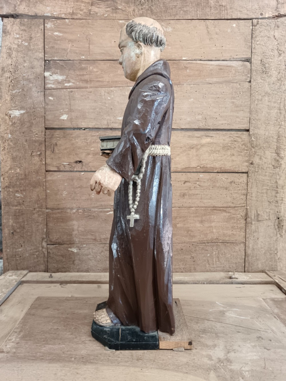 An antique carved wooden figure depicting Saint Anthony wearing a dark brown habit and holding a book. View V