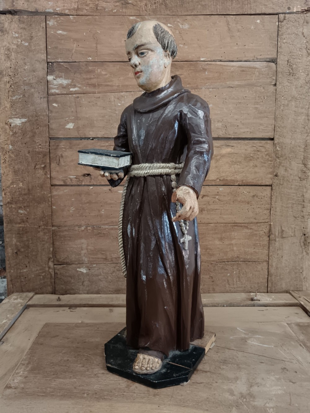 An antique carved wooden figure depicting Saint Anthony wearing a dark brown habit and holding a book. View VI