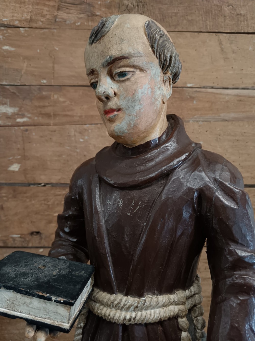 An antique carved wooden figure depicting Saint Anthony wearing a dark brown habit and holding a book. View VII