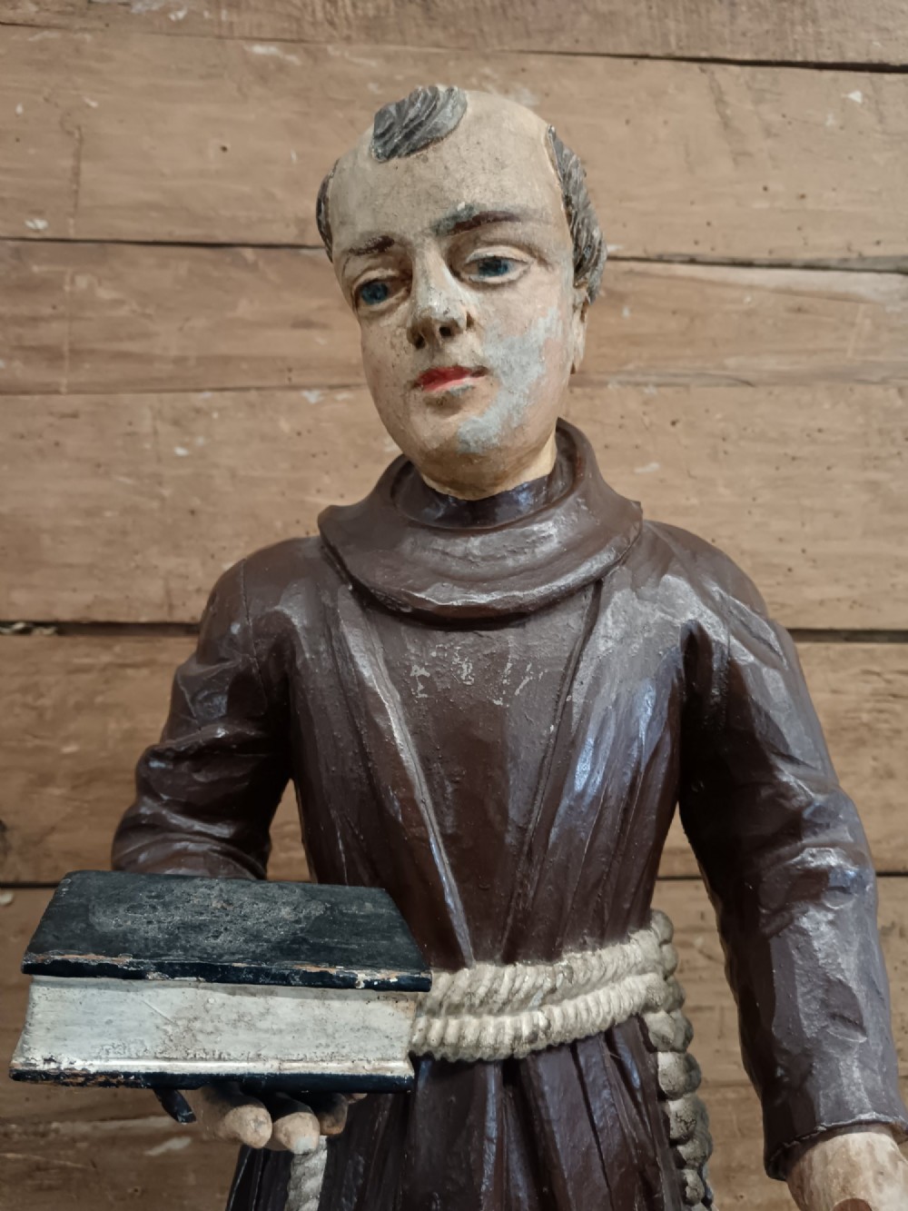 An antique carved wooden figure depicting Saint Anthony wearing a dark brown habit and holding a book. View IX