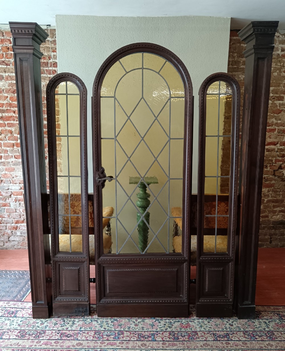 An antique dark wood vestibule doorway featuring a central arched leaded glass door flanked by two slender side lights and classic fluted columns. View II