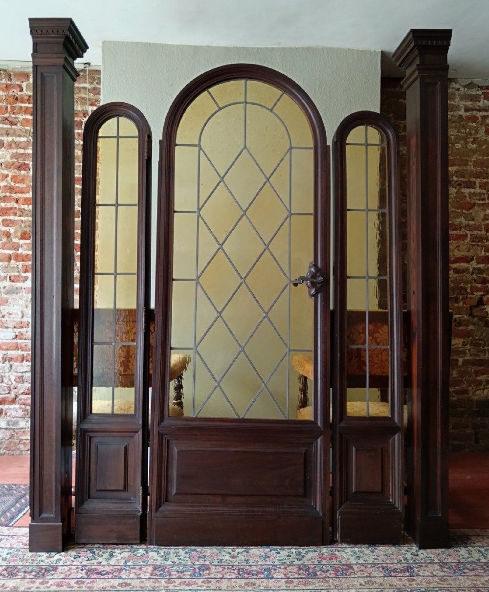 An antique dark wood vestibule doorway featuring a central arched leaded glass door flanked by two slender side lights and classic fluted columns. View III