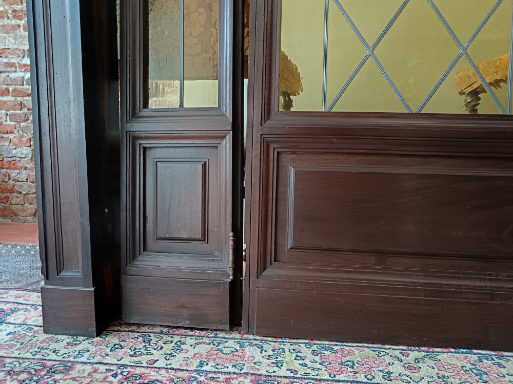 An antique dark wood vestibule doorway featuring a central arched leaded glass door flanked by two slender side lights and classic fluted columns. View IV