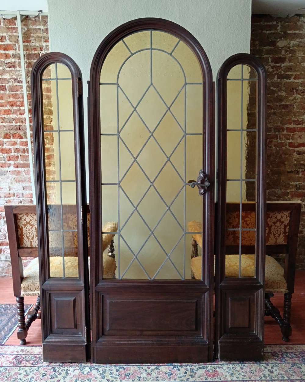 An antique dark wood vestibule doorway featuring a central arched leaded glass door flanked by two slender side lights and classic fluted columns. View X