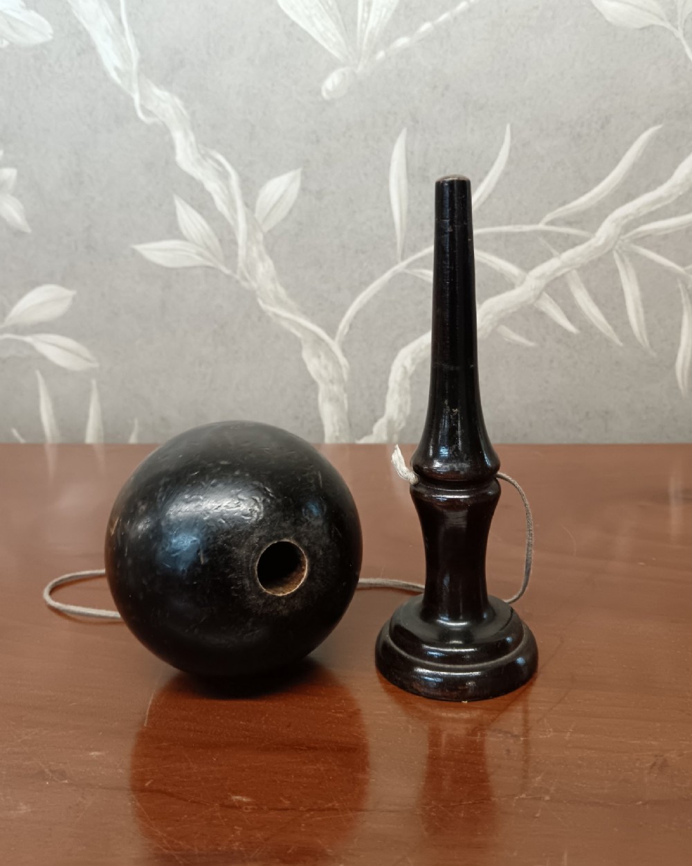 An antique ebonised turned wooden bilboquet cup and ball game resting upright on a polished surface. View II