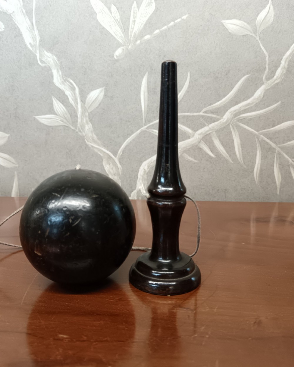 An antique ebonised turned wooden bilboquet cup and ball game resting upright on a polished surface. View III