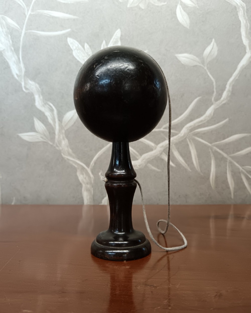 An antique ebonised turned wooden bilboquet cup and ball game resting upright on a polished surface.