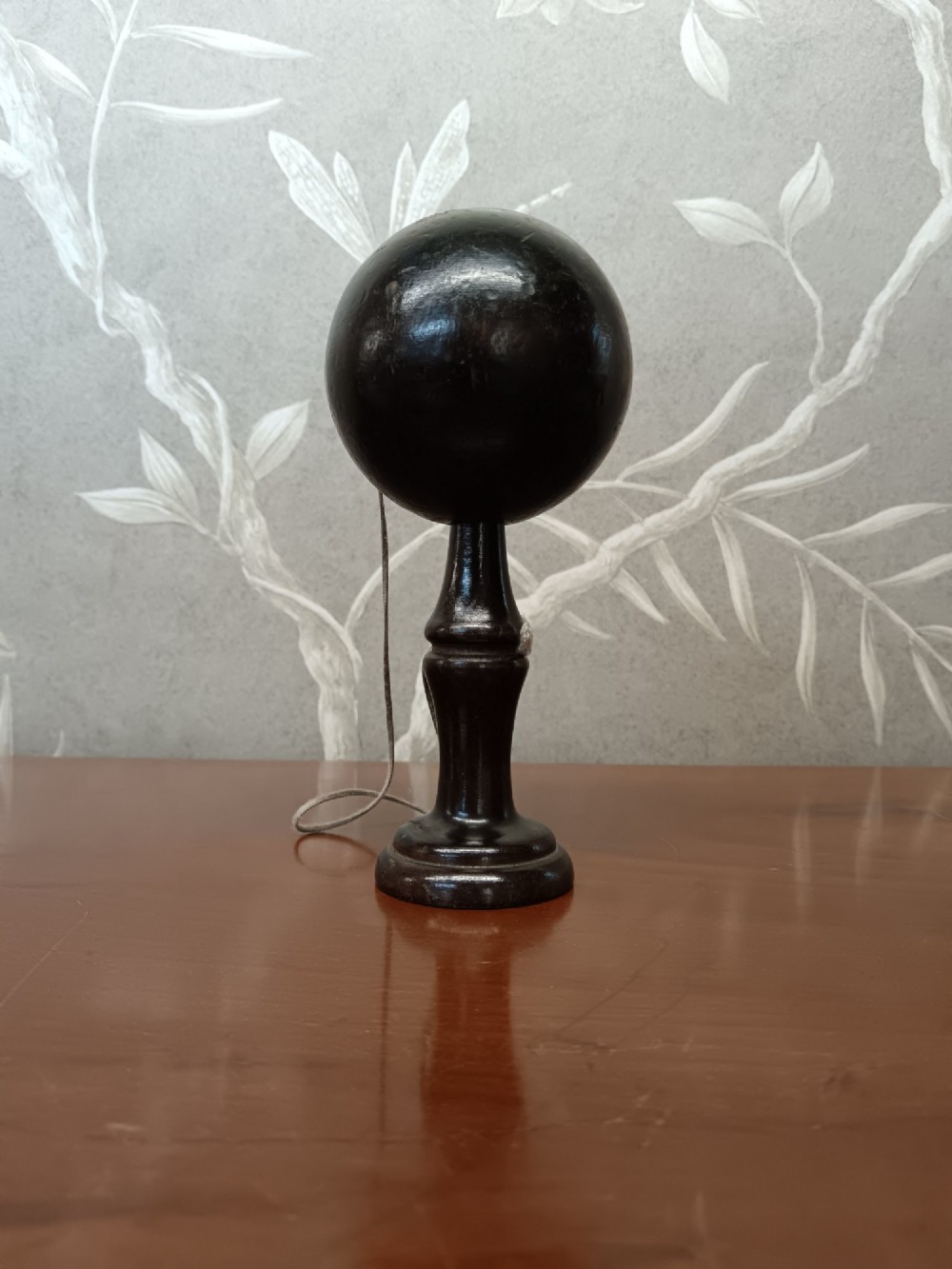 An antique ebonised turned wooden bilboquet cup and ball game resting upright on a polished surface. View IV