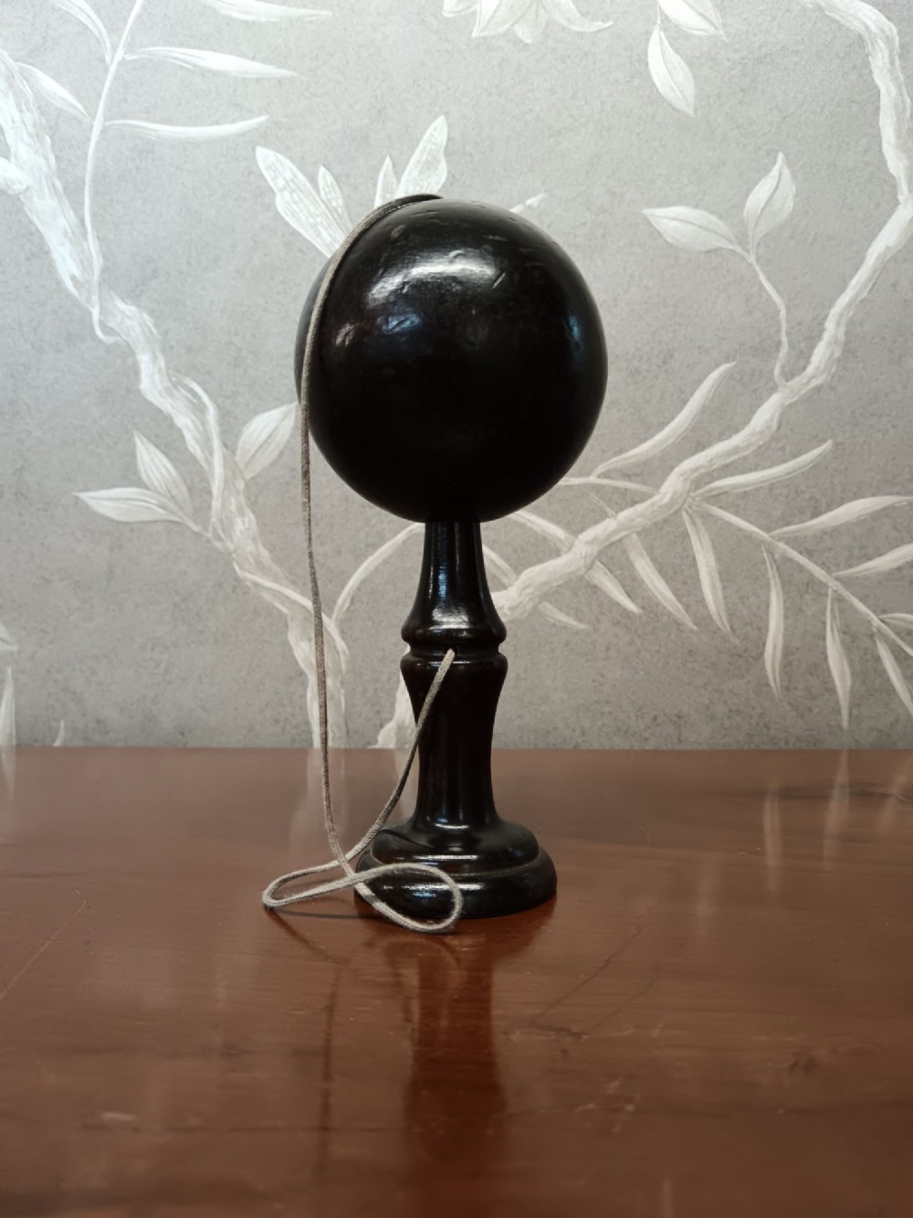 An antique ebonised turned wooden bilboquet cup and ball game resting upright on a polished surface. View V