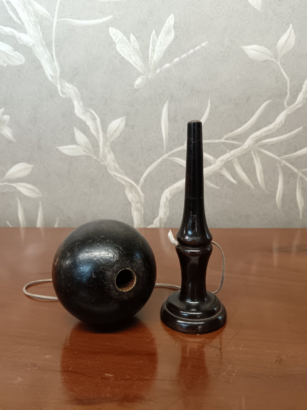 An antique ebonised turned wooden bilboquet cup and ball game resting upright on a polished surface. View VI