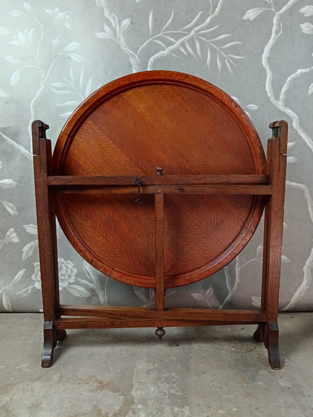 An antique oak folding card table with a circular reversible top supported by an interlocking wooden base. View II