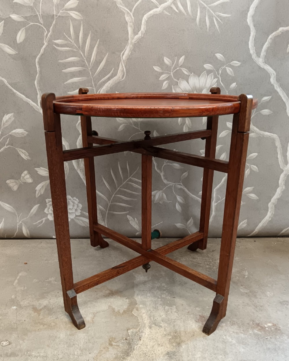 An antique oak folding card table with a circular reversible top supported by an interlocking wooden base.