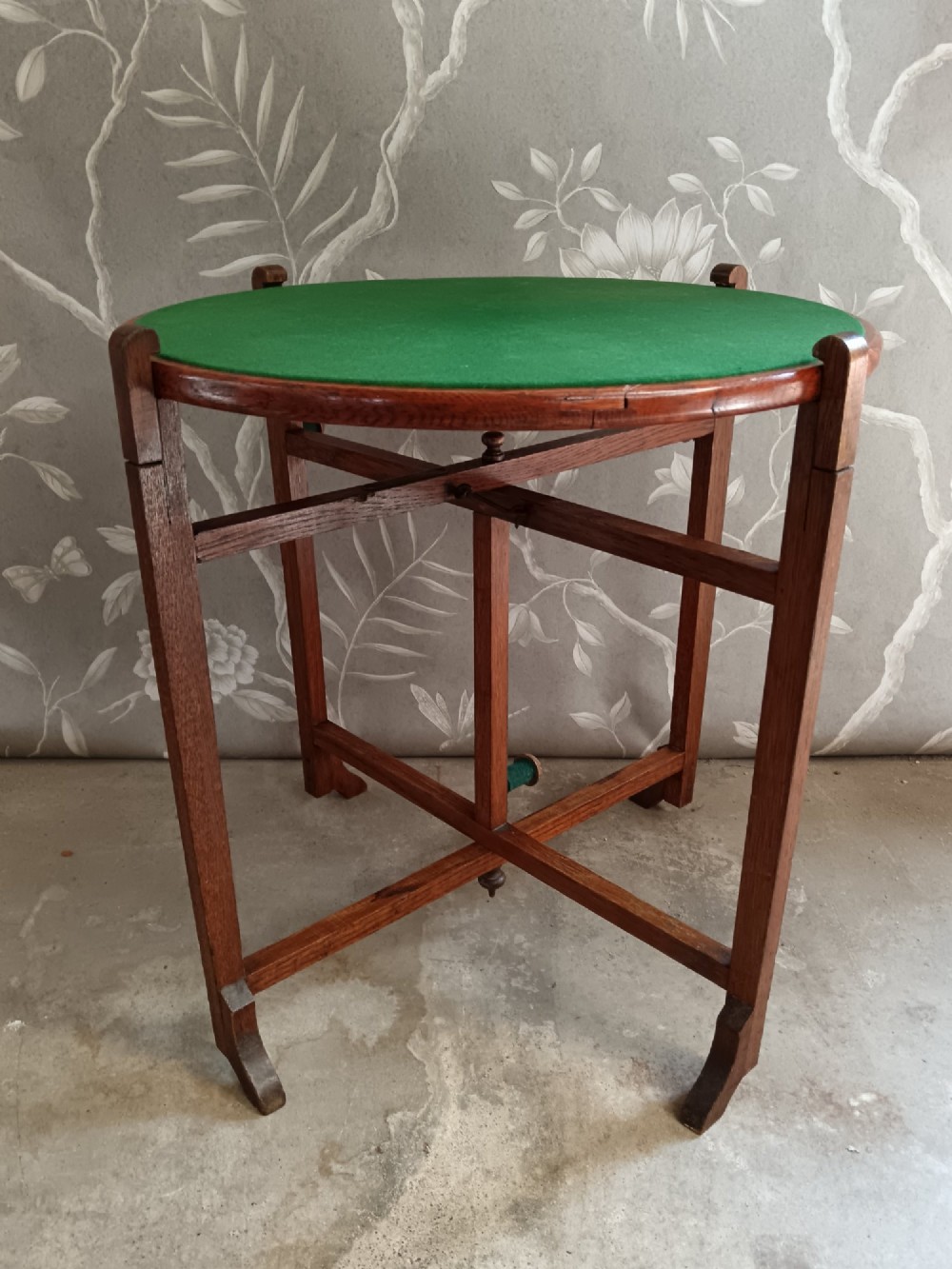 An antique oak folding card table with a circular reversible top supported by an interlocking wooden base. View VI