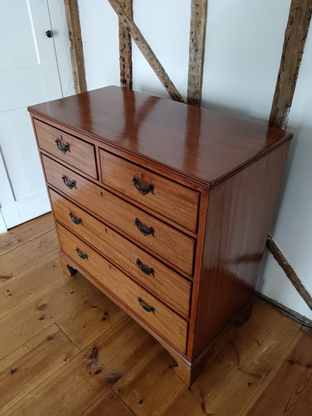 A Georgian mahogany chest of drawers featuring two short drawers above three full-width graduated drawers with brass drop handles and bracket feet. View V