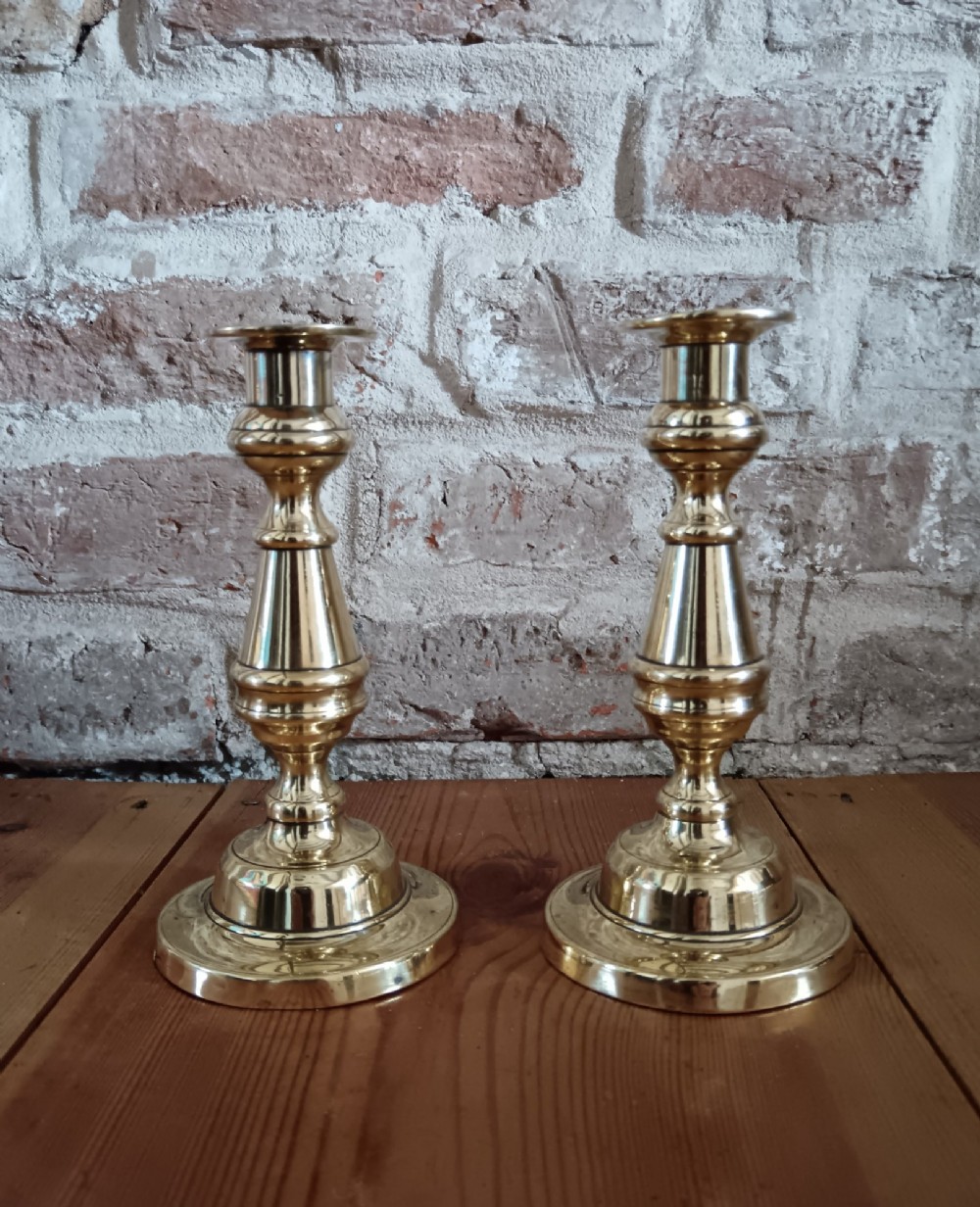 A pair of polished turned brass candlesticks featuring circular stepped bases and baluster stems. View II