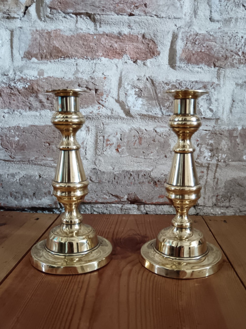 A pair of polished turned brass candlesticks featuring circular stepped bases and baluster stems. View III