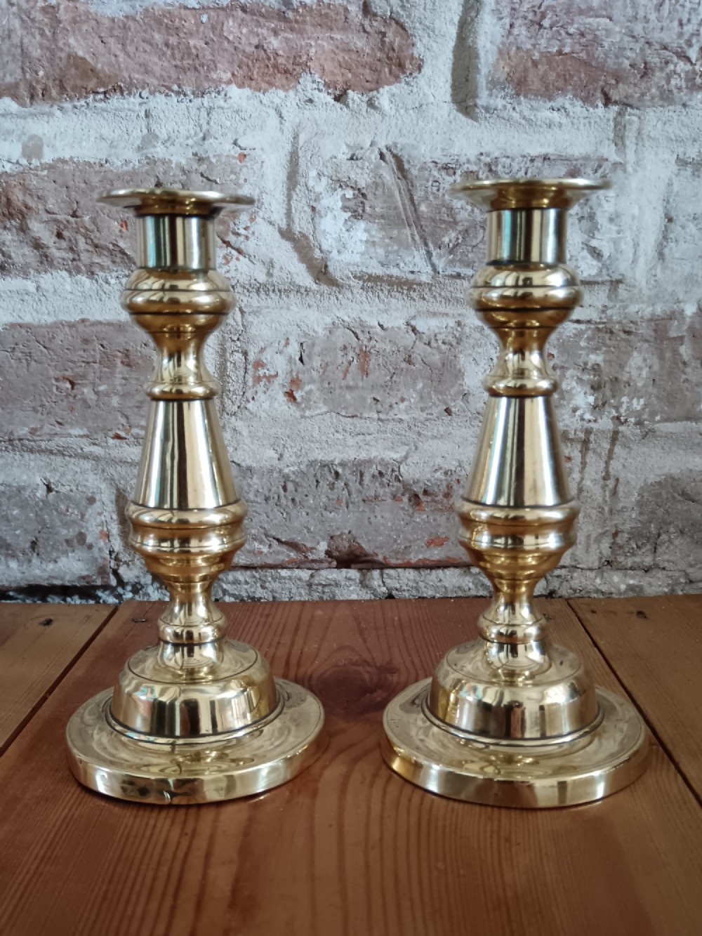 A pair of polished turned brass candlesticks featuring circular stepped bases and baluster stems. View IV