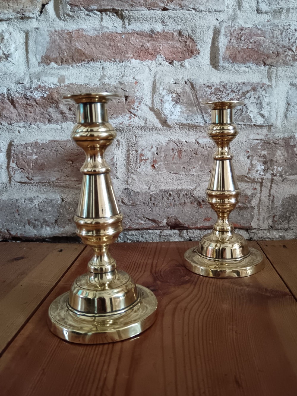 A pair of polished turned brass candlesticks featuring circular stepped bases and baluster stems. View V
