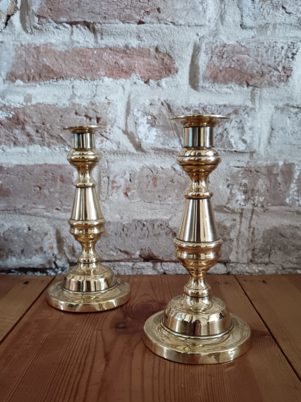 A pair of polished turned brass candlesticks featuring circular stepped bases and baluster stems.
