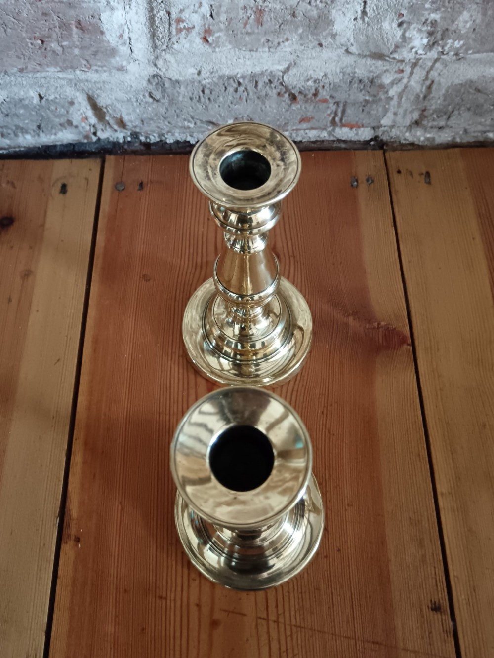 A pair of polished turned brass candlesticks featuring circular stepped bases and baluster stems. View VII
