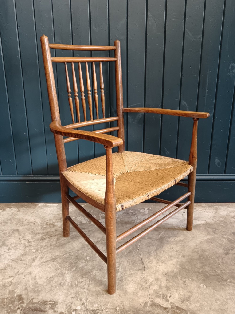 A late 19th-century Arts and Crafts Sussex armchair with a spindle backrest, curved armrests, turned legs, and a natural rush seat.