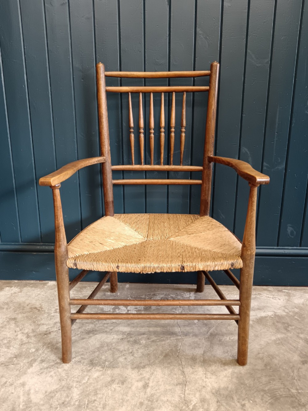 A late 19th-century Arts and Crafts Sussex armchair with a spindle backrest, curved armrests, turned legs, and a natural rush seat. View II