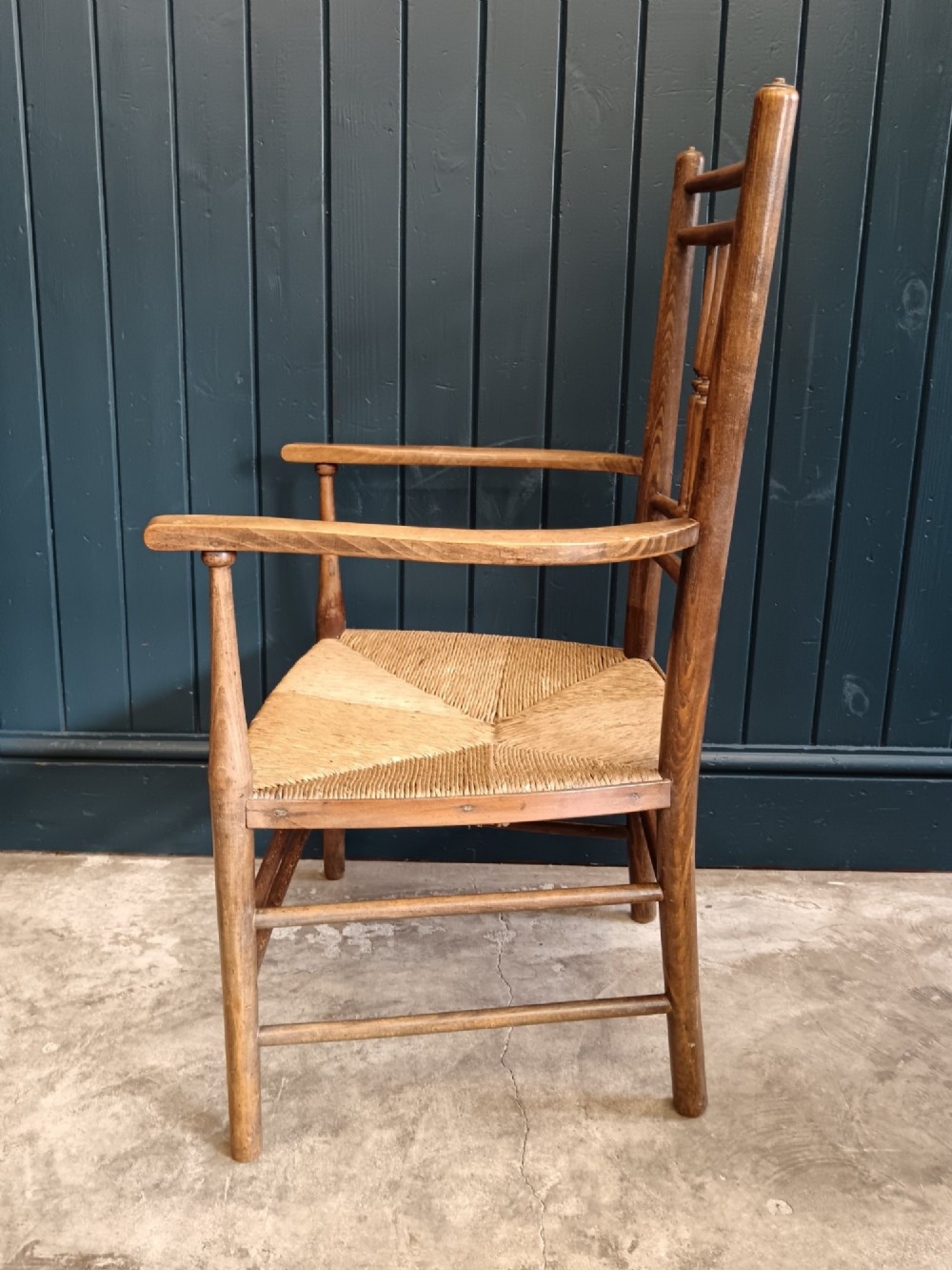A late 19th-century Arts and Crafts Sussex armchair with a spindle backrest, curved armrests, turned legs, and a natural rush seat. View IV
