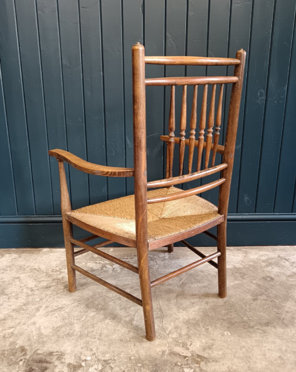 A late 19th-century Arts and Crafts Sussex armchair with a spindle backrest, curved armrests, turned legs, and a natural rush seat. View V