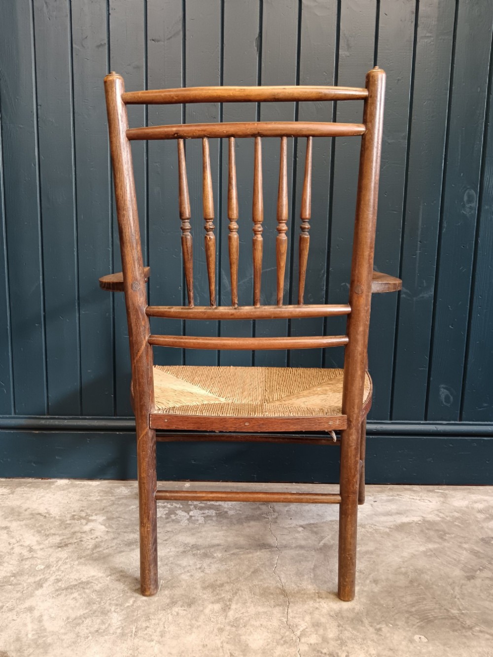 A late 19th-century Arts and Crafts Sussex armchair with a spindle backrest, curved armrests, turned legs, and a natural rush seat. View VI