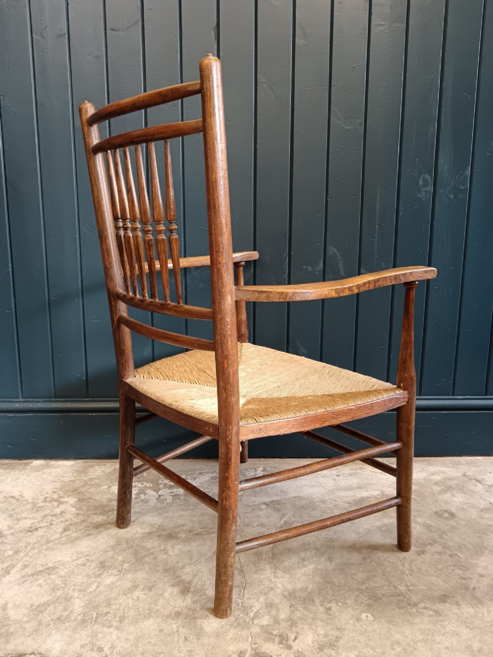A late 19th-century Arts and Crafts Sussex armchair with a spindle backrest, curved armrests, turned legs, and a natural rush seat. View VII