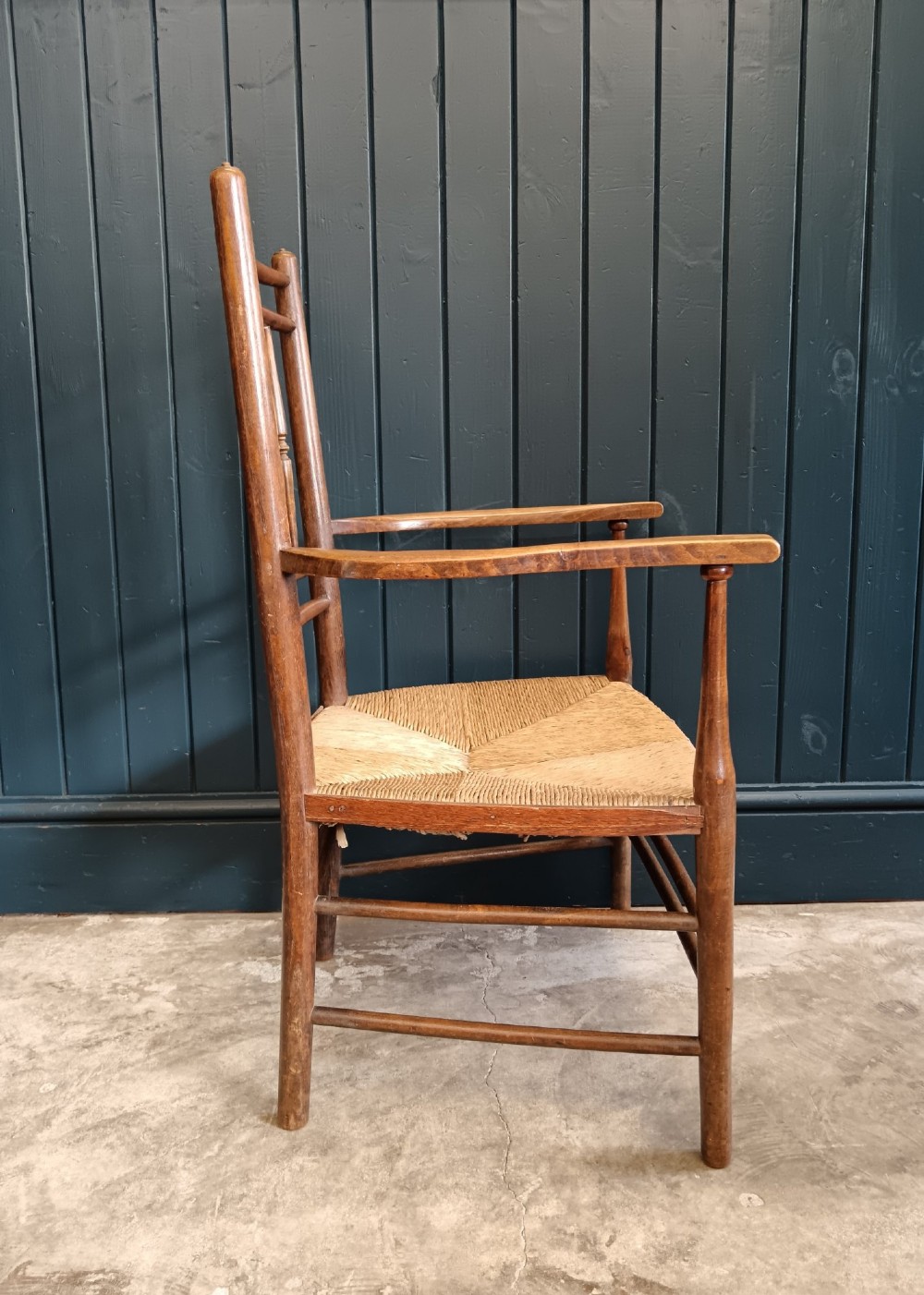 A late 19th-century Arts and Crafts Sussex armchair with a spindle backrest, curved armrests, turned legs, and a natural rush seat. View VIII
