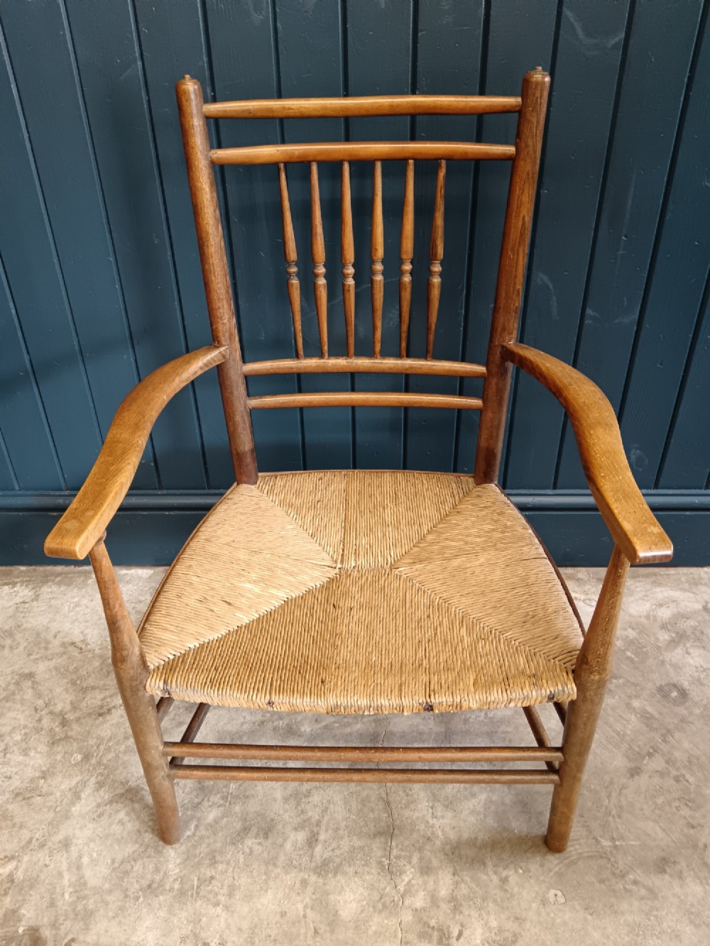 A late 19th-century Arts and Crafts Sussex armchair with a spindle backrest, curved armrests, turned legs, and a natural rush seat. View IX
