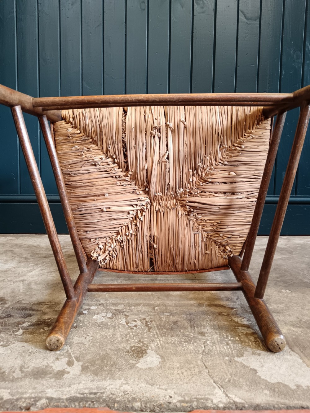 A late 19th-century Arts and Crafts Sussex armchair with a spindle backrest, curved armrests, turned legs, and a natural rush seat. View X