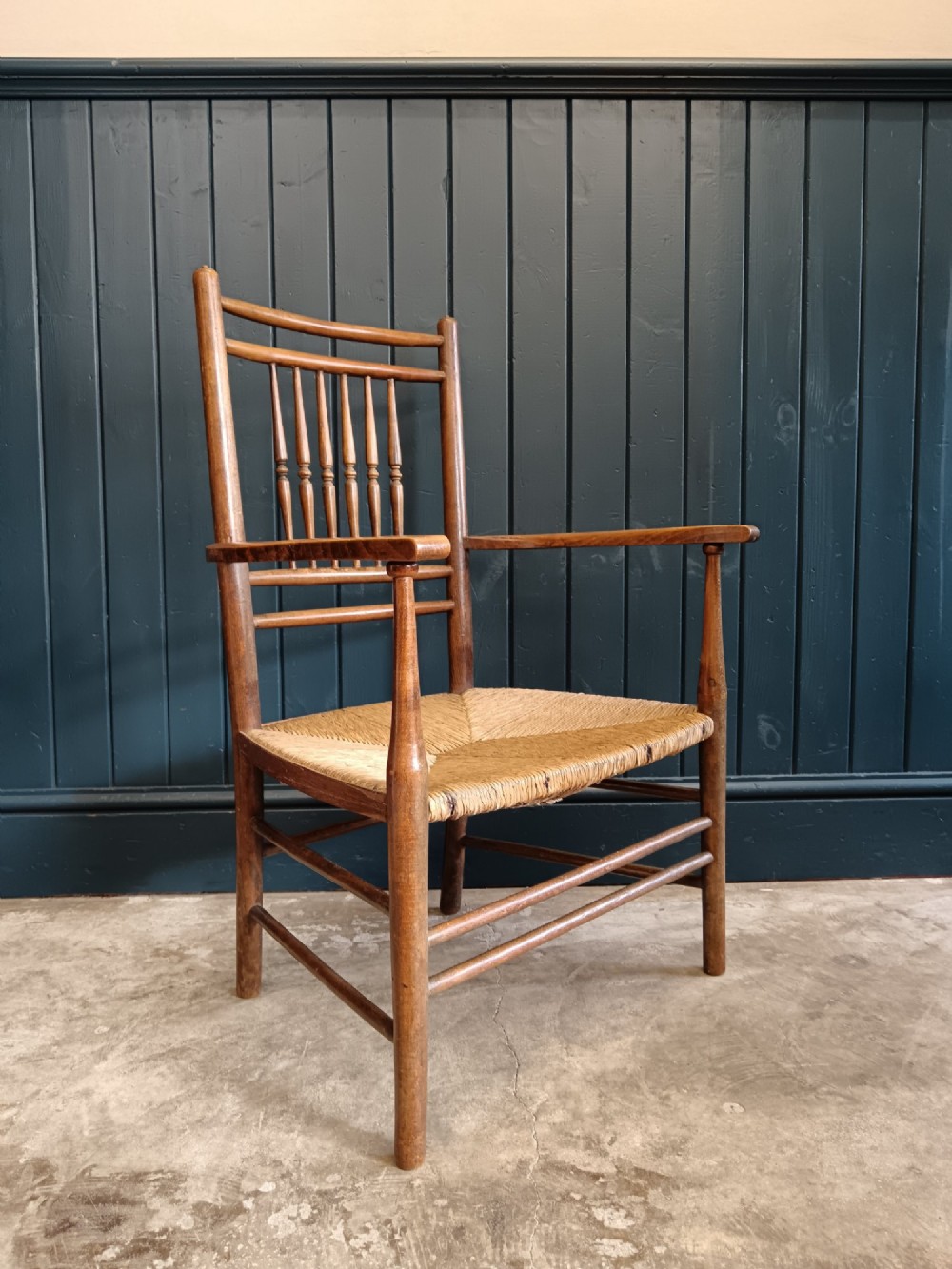 A late 19th-century Arts and Crafts Sussex armchair with a spindle backrest, curved armrests, turned legs, and a natural rush seat. View XII