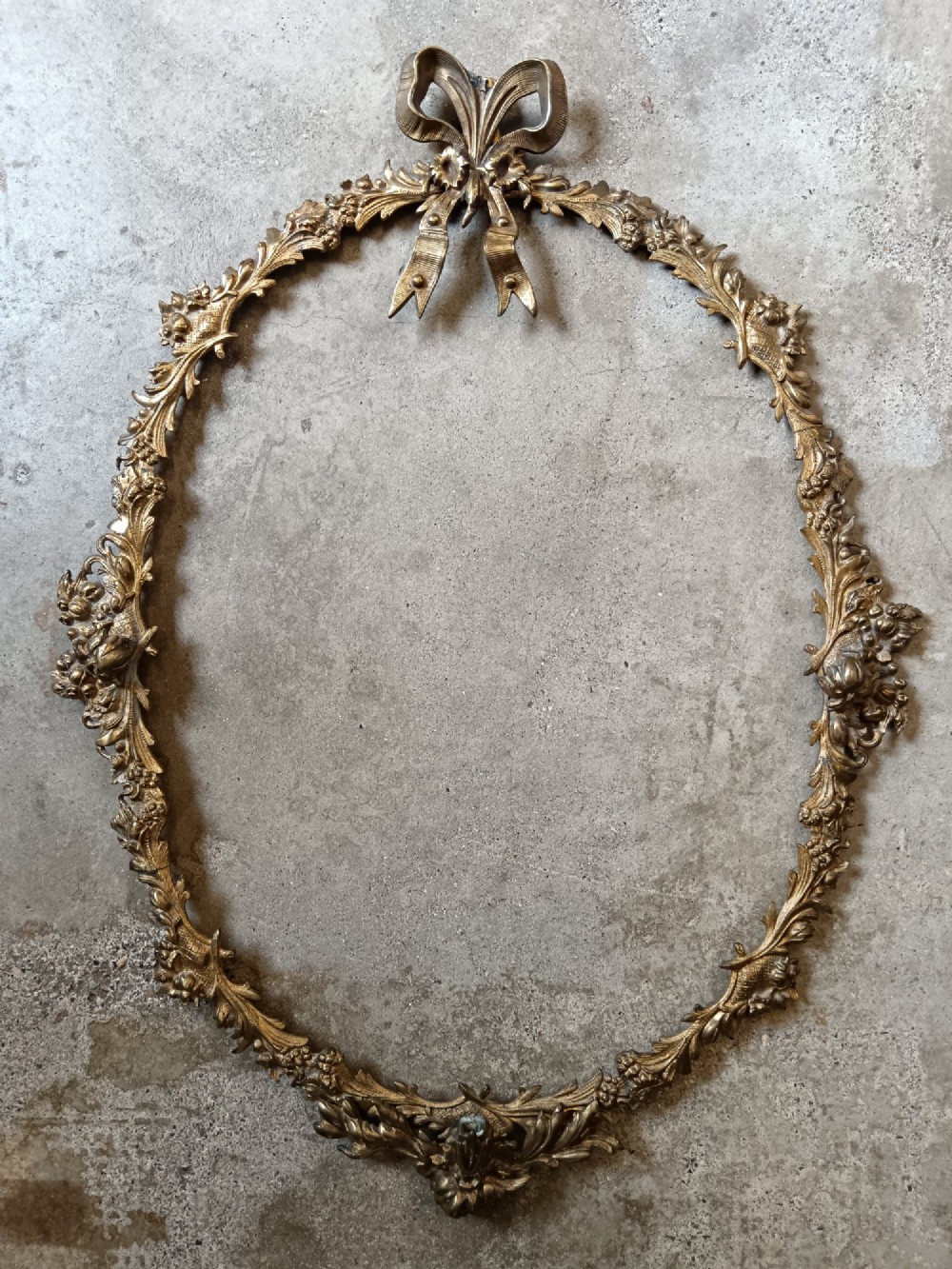 An oval gilt bronze wall mirror with a detailed floral foliate frame and a ribbon bow cresting at the top. View IV