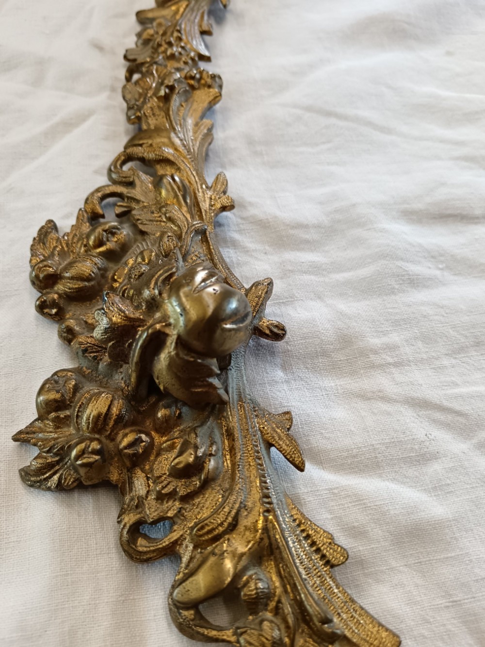An oval gilt bronze wall mirror with a detailed floral foliate frame and a ribbon bow cresting at the top. View IX