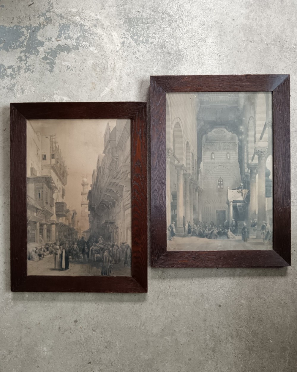 A pair of 19th-century sepia lithographs depicting architectural street and interior scenes of Cairo, mounted in dark oak frames.