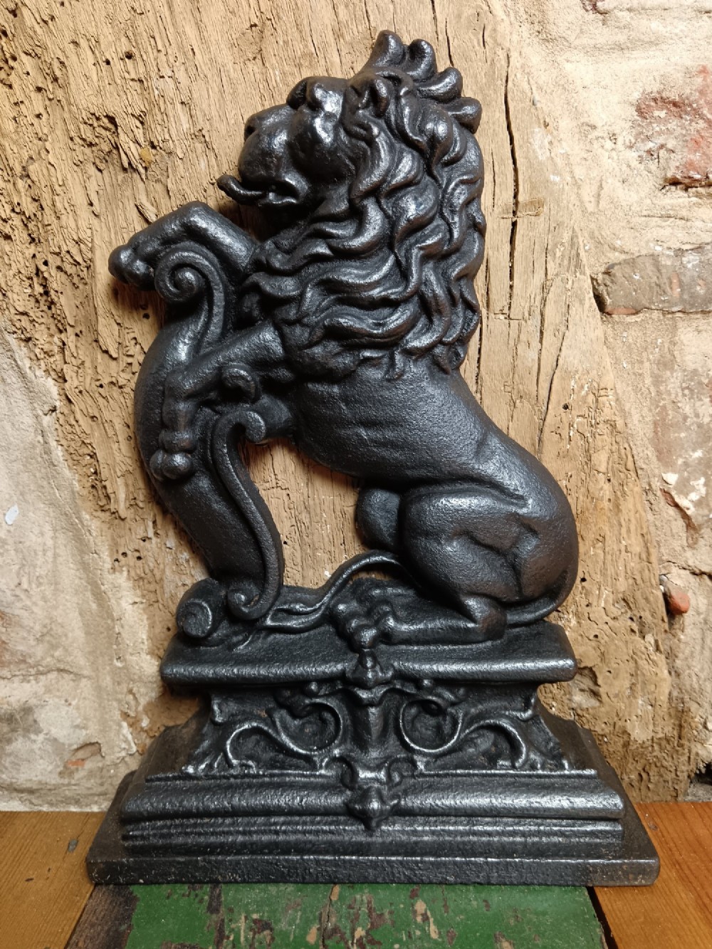A black cast iron doorstop depicting a heraldic lion rampant seated on a decorated scrollwork base.