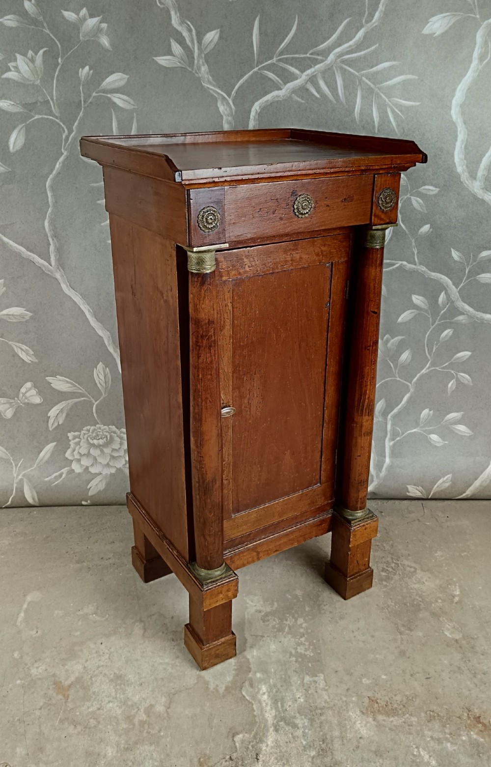 A nineteenth-century Italian Empire walnut bedside cabinet featuring a top drawer, single panelled door, brass rosette mounts, and flanking column columns. View III