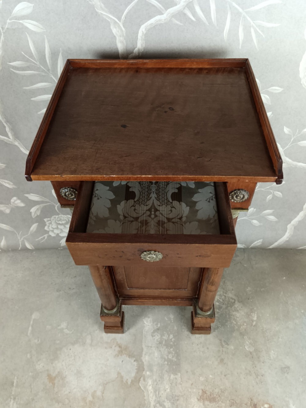 A nineteenth-century Italian Empire walnut bedside cabinet featuring a top drawer, single panelled door, brass rosette mounts, and flanking column columns. View V