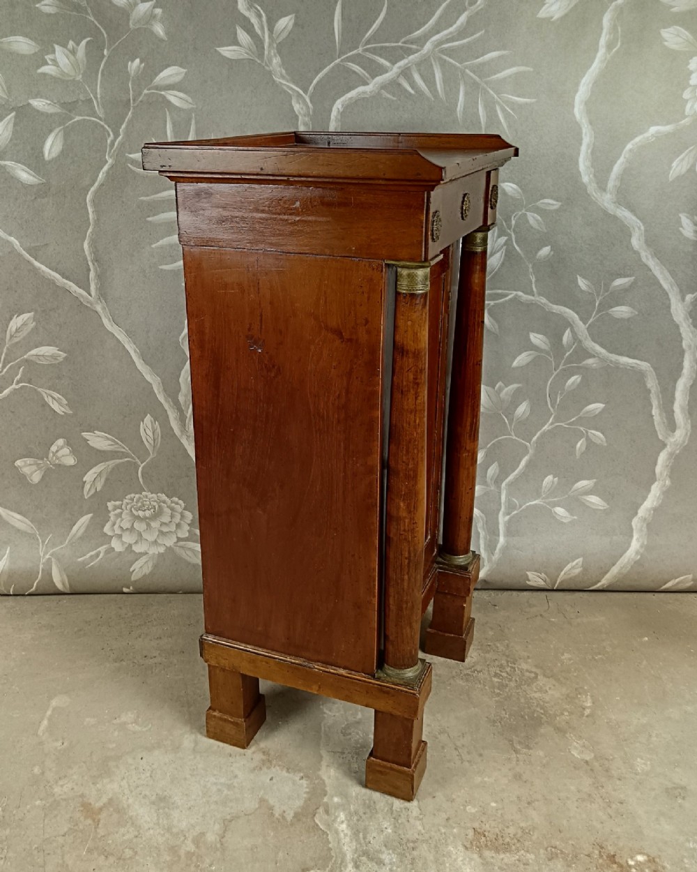 A nineteenth-century Italian Empire walnut bedside cabinet featuring a top drawer, single panelled door, brass rosette mounts, and flanking column columns. View IX