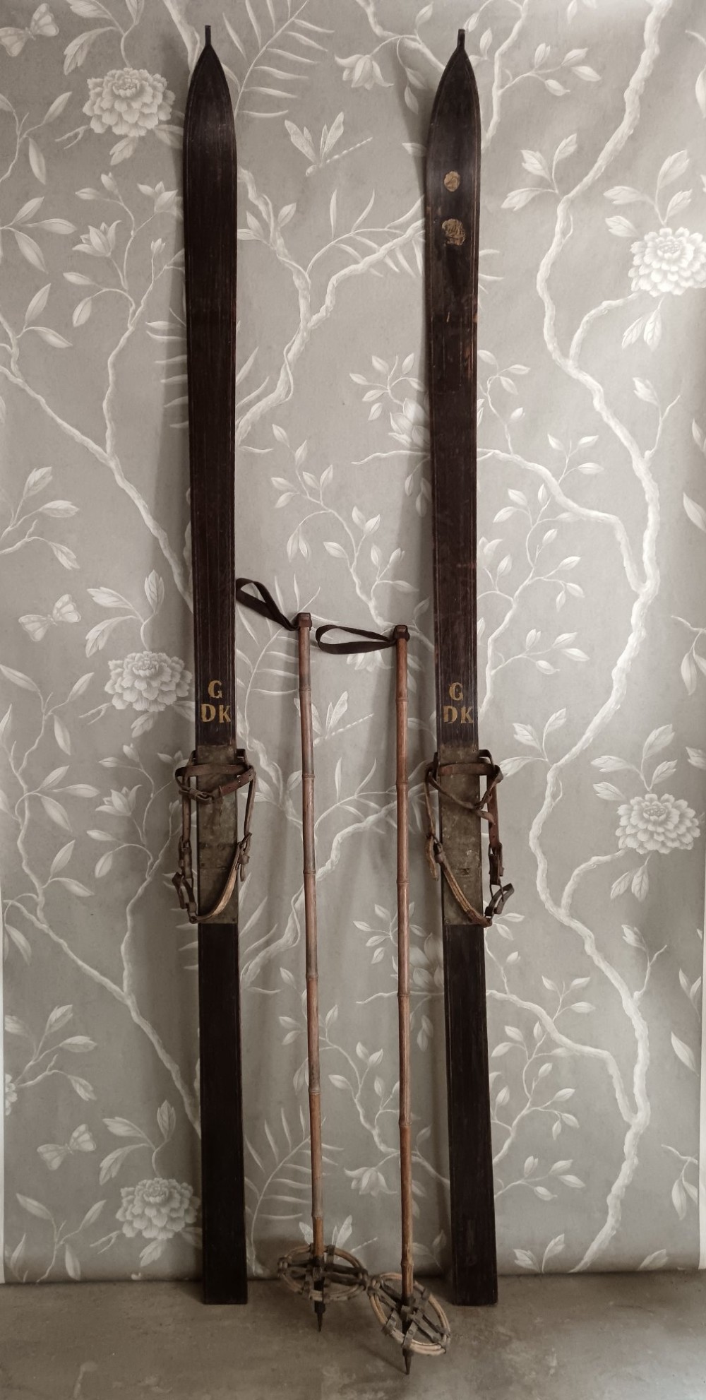 A pair of dark wood turn-of-the-century Norwegian skis accompanied by bamboo ski poles with leather bindings and cane baskets.