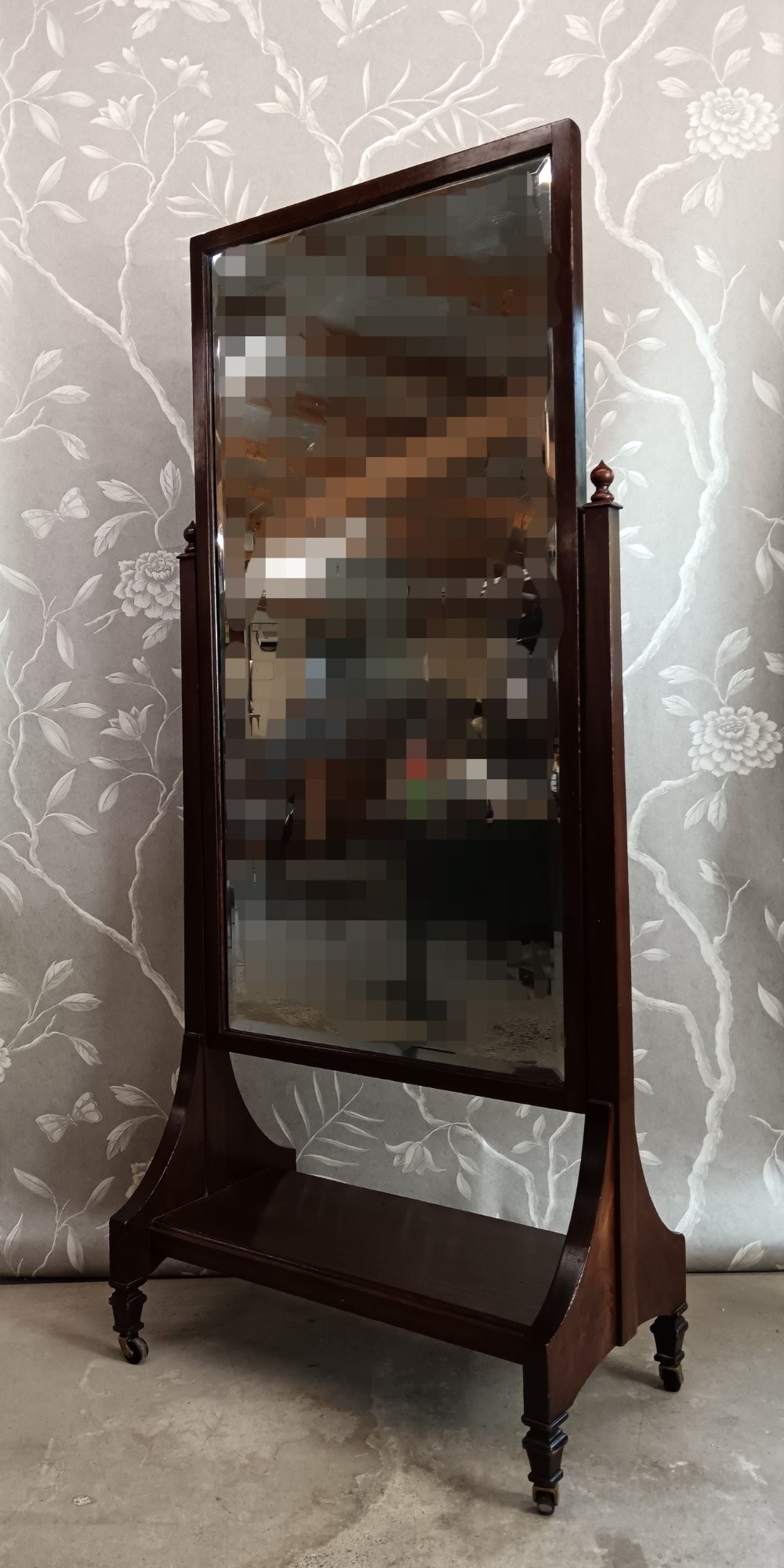 A late Victorian mahogany cheval mirror featuring a rectangular full-length pivoting frame set between turned finial posts on a shelf base with brass castors.