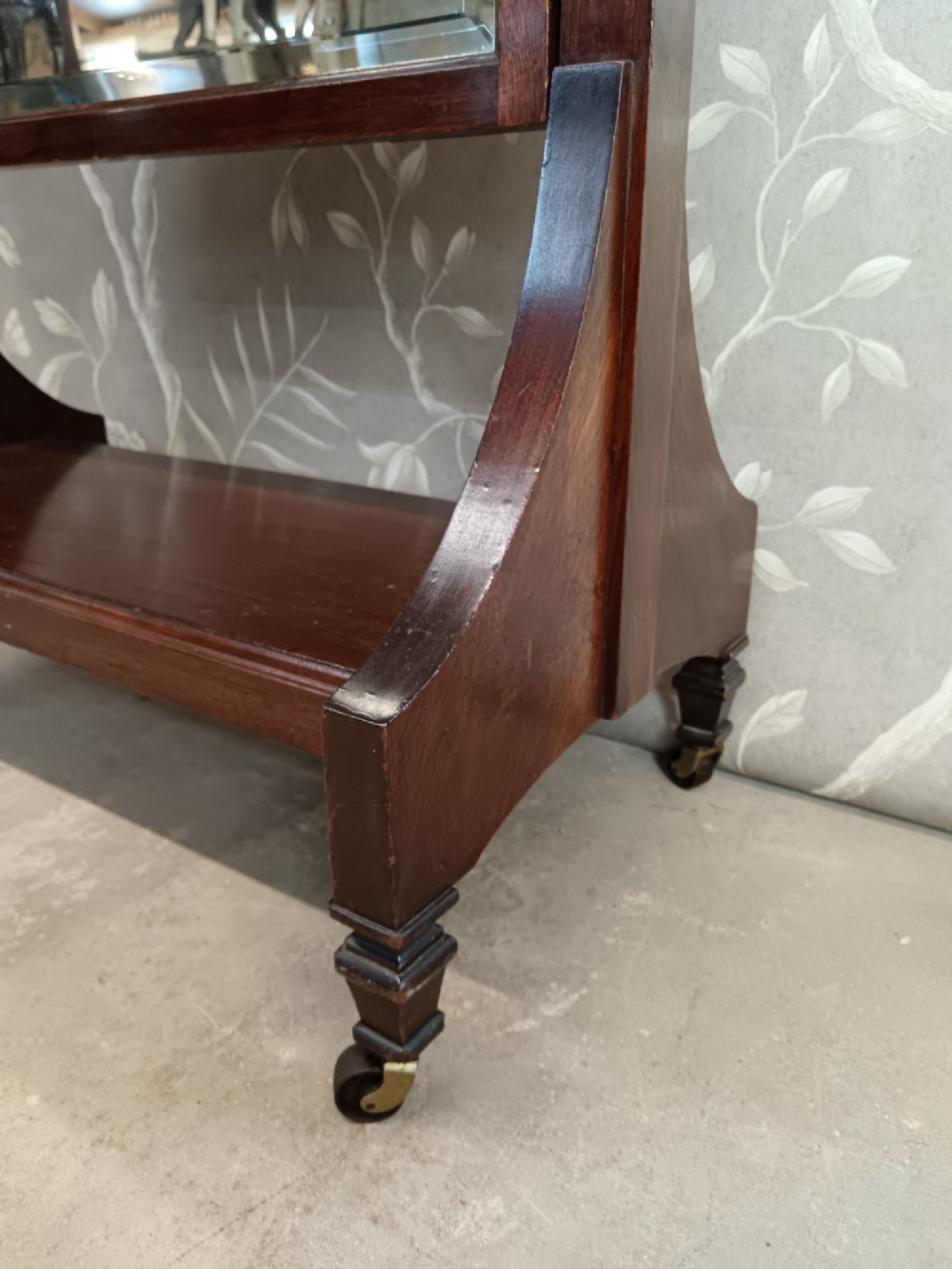 A late Victorian mahogany cheval mirror featuring a rectangular full-length pivoting frame set between turned finial posts on a shelf base with brass castors. View III