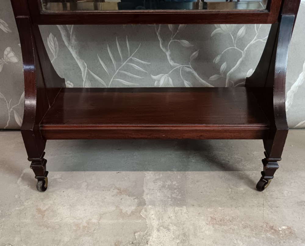 A late Victorian mahogany cheval mirror featuring a rectangular full-length pivoting frame set between turned finial posts on a shelf base with brass castors. View IV