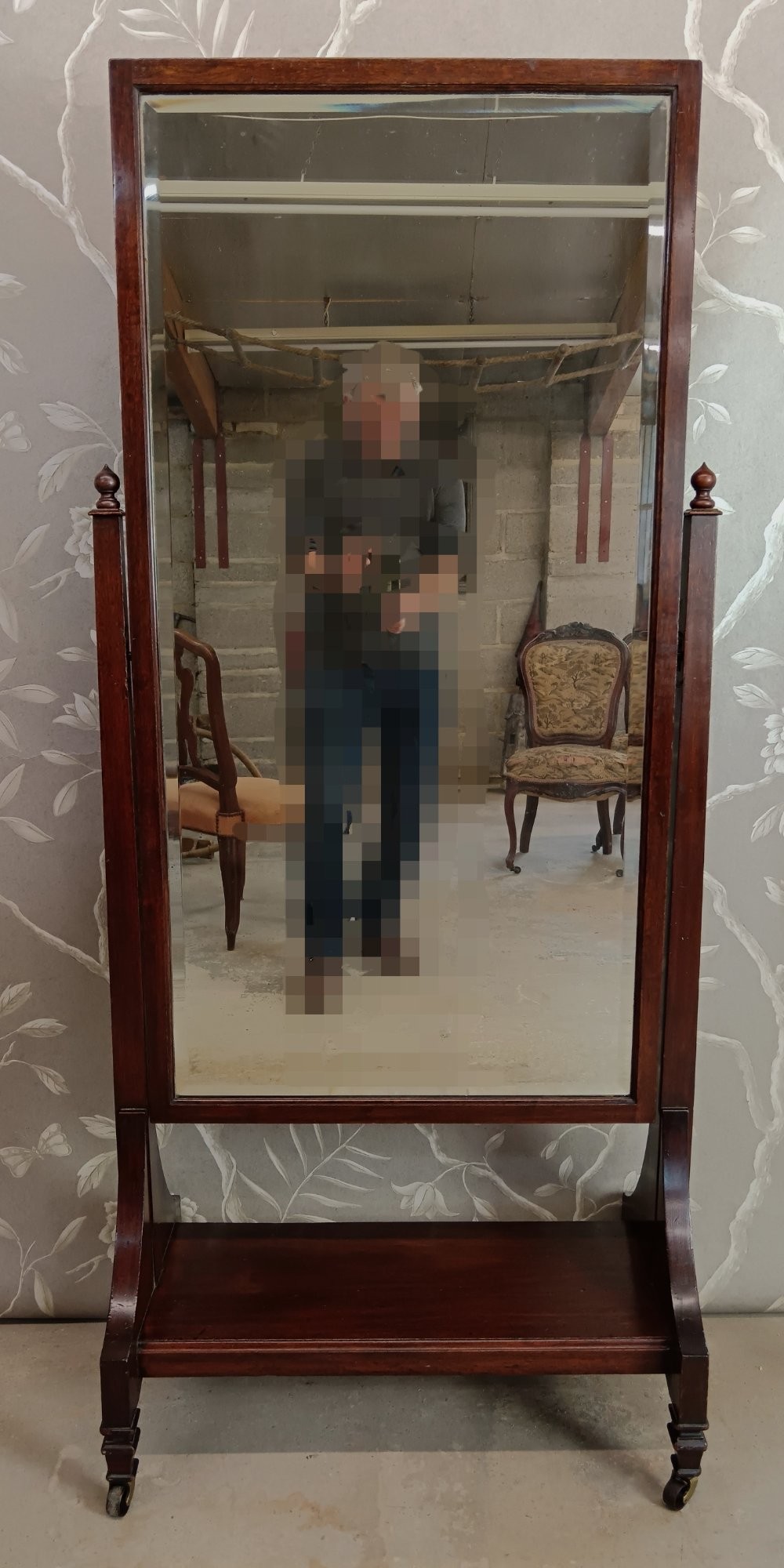 A late Victorian mahogany cheval mirror featuring a rectangular full-length pivoting frame set between turned finial posts on a shelf base with brass castors. View VI